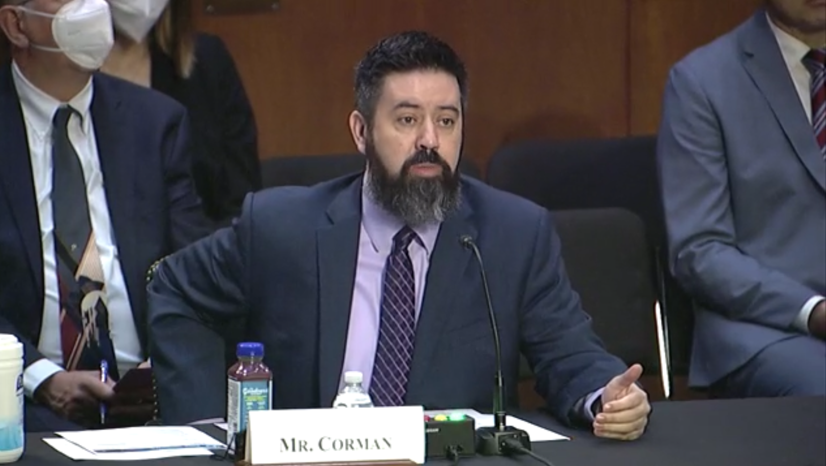 Josh Corman sits at a table with a microphone before a Senate Committee.